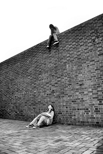 Two girls looking at each other - one sitting on top of high brick wall, one sitting on ground below